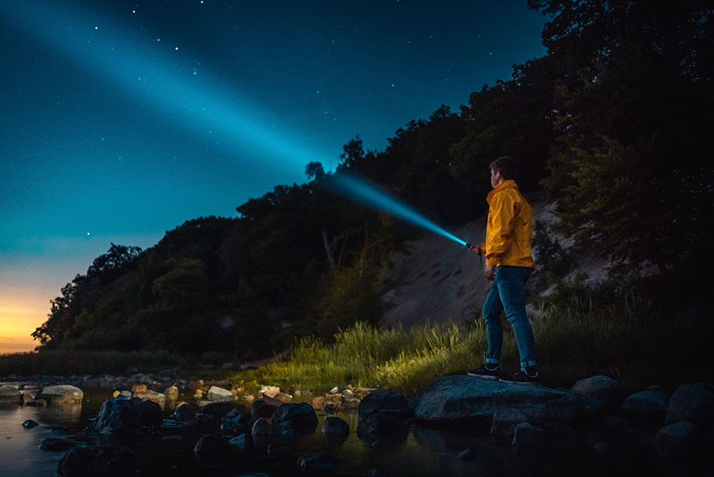 Eine männliche Person leuchtet mit einer Taschenlampe in den Nachthimmel. 