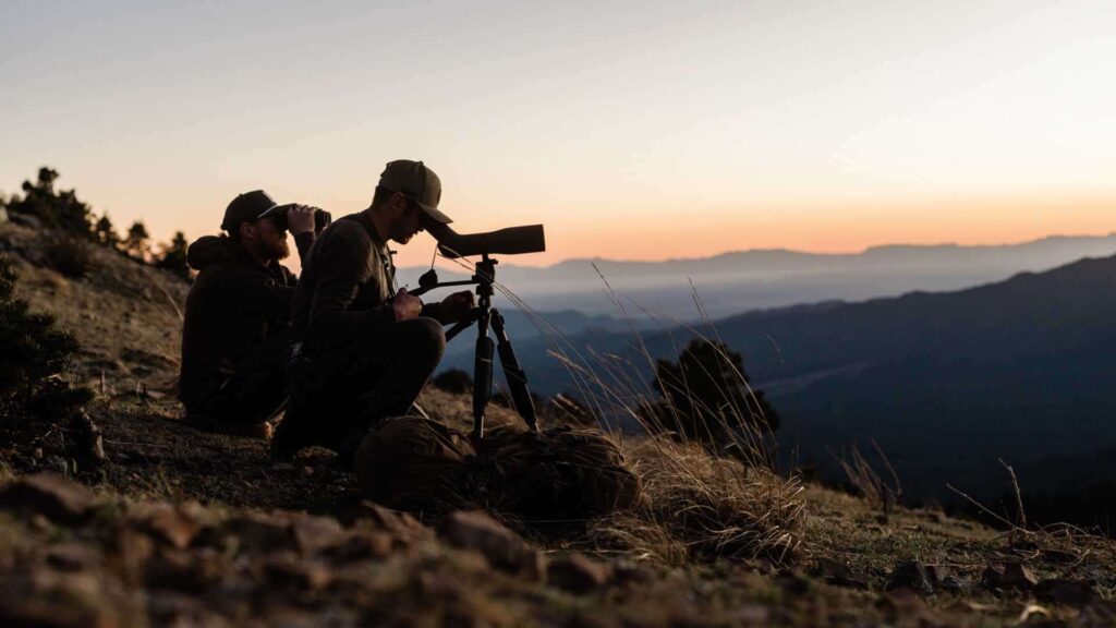 Zwei Naturbeobachter nutzen bei Sonnenuntergang Fernglas und Swarovski AT Endura 75 Spektiv in einer Berglandschaft.